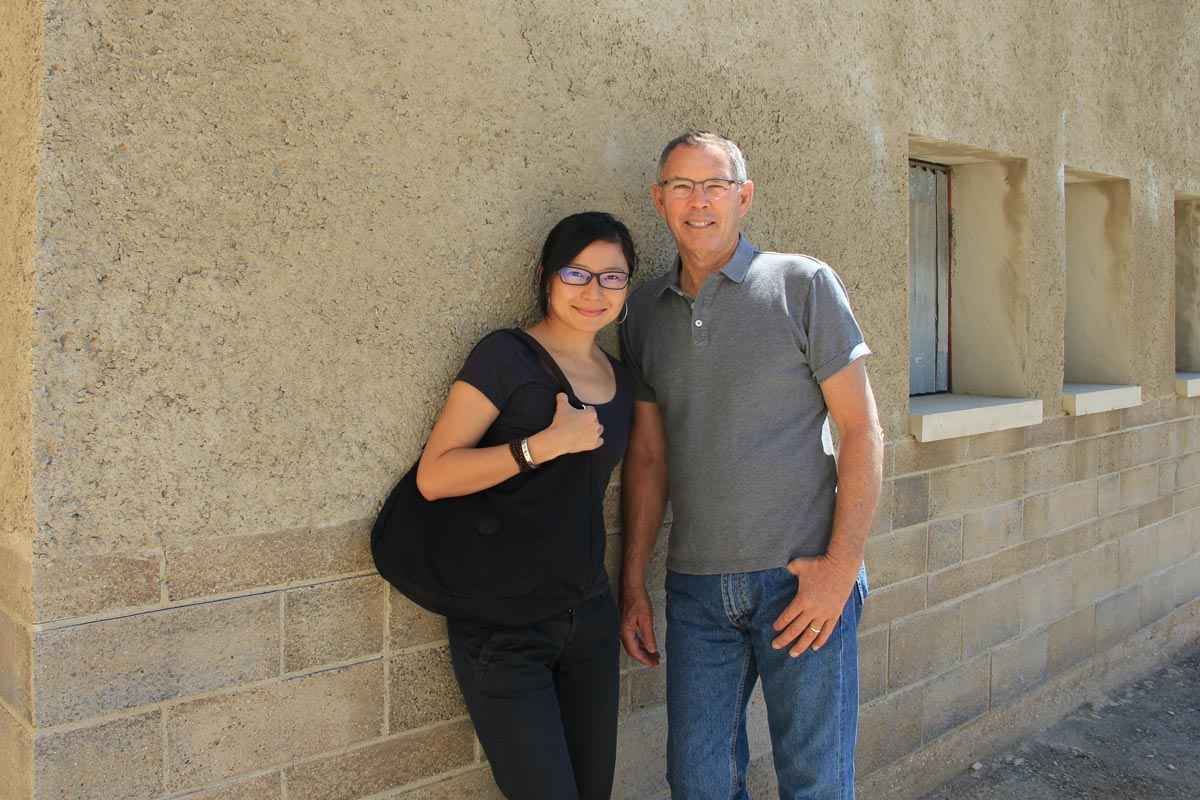 Dr. Rongrong Hu and David Easton at the Watershed Materials headquarters, standing in front of a building made with rammed earth Watershed Block below rammed earth PISE.