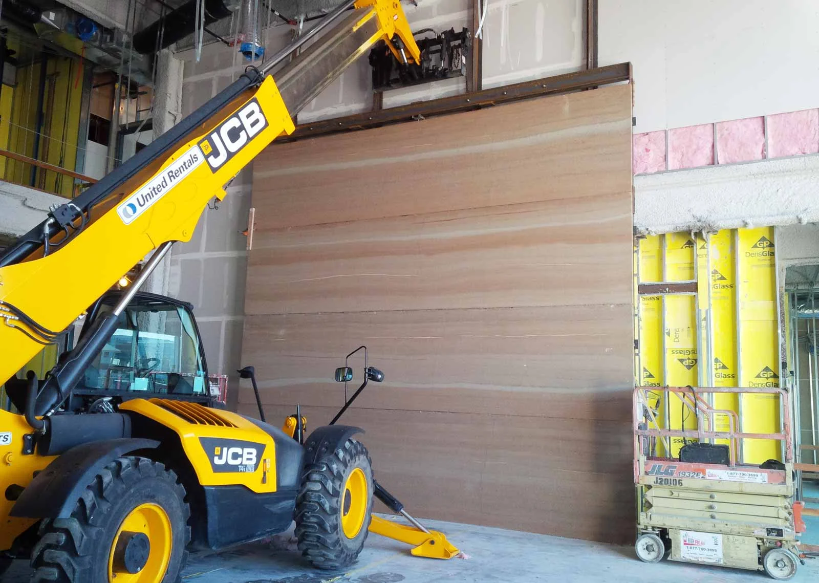 For the installation of the four big Stadium TechCenter panels, we used a long reach forklift to set the panels rather than a crane because the roof was already on the building. The forklift picked each of the twenty-two foot long by five foot high panels off the truck, backed directly into the lobby with only inches to clear the door frames, executed a ninety-degree turn and placed the panels one on top of another against four steel posts where they were welded in place.