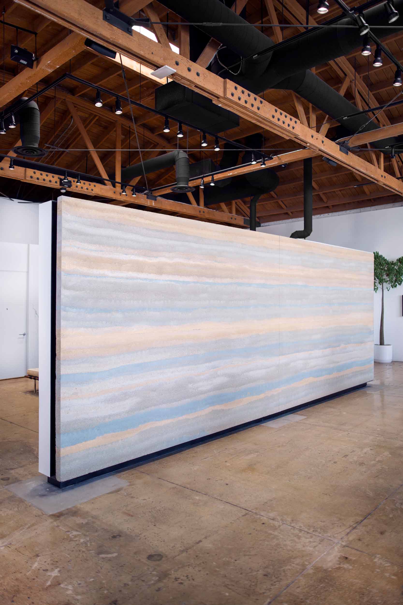 The interior of newest Reformation store, located a few blocks east of Beverly Hills, features a 200 square foot free-standing mural of stratified rammed earth floating above a polished reclaimed concrete slab - nearly naked. These thin slabs of rammed earth are like nothing else. Everywhere in the world, rammed earth walls are thick, massively heavy, and constructed right at their final resting place. Making rammed earth thin enough to put on a truck, carry into a building, and hang on a wall is a paradigm shift for the earth building industry. Image © Jesse Gillan