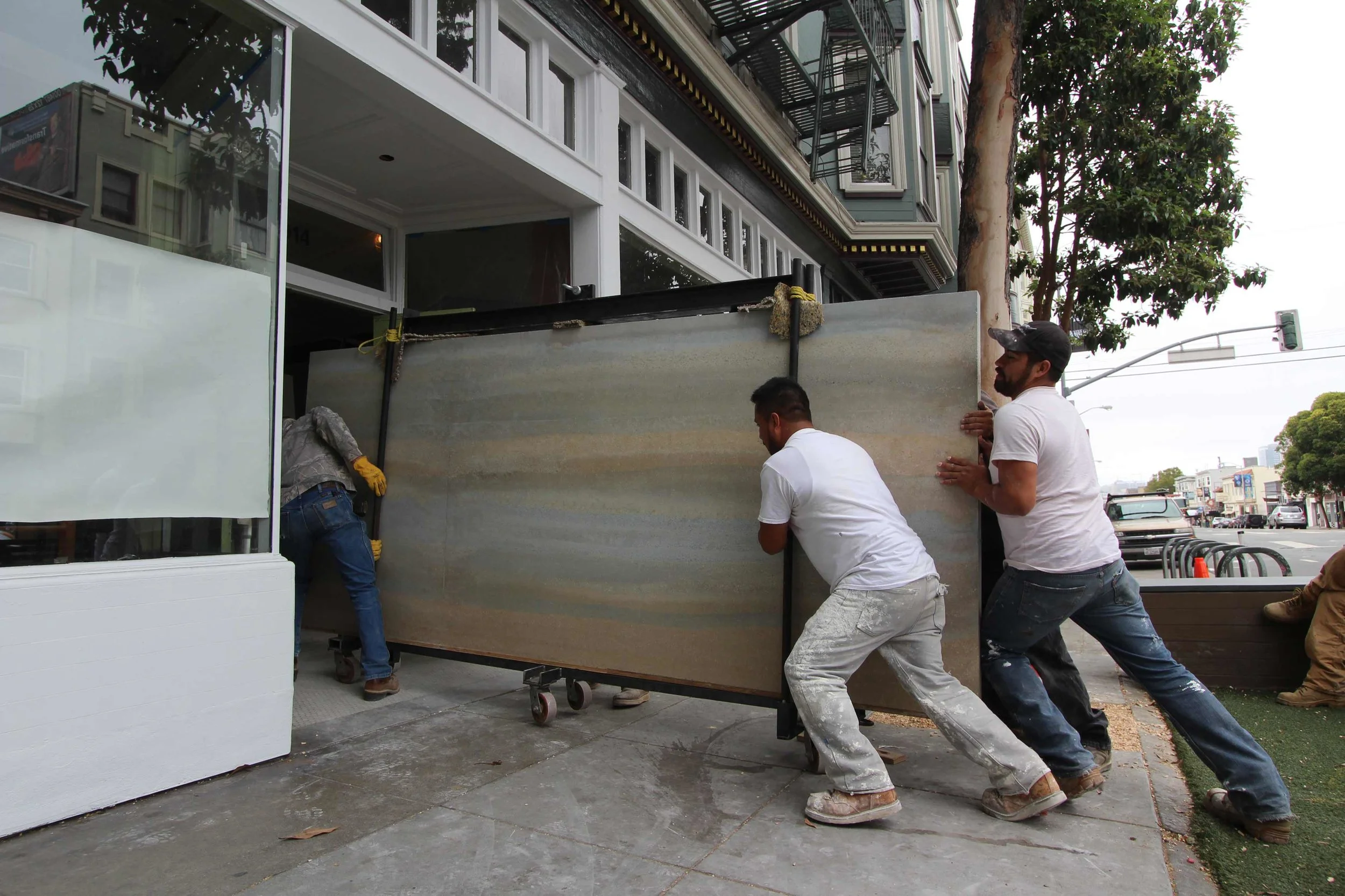 Pre-cast interior rammed earth panels being delivered to the new Reformation store in the Mission district of San Francisco. To accomplish the delivery - which had to be made through the storefront's narrow front door with no room for a forklift or crane - we built a portable jib to transfer each 2,000 pound panel from the trailer to the sidewalk and we built a six-wheeled trolley to roll the panels into the store. As you can see, it took three people pushing and one pulling to get the panel up and over the door threshold. The rammed earth arrived safe and ready for installation in a retail store that could have never used the material with traditional on-site form setting methods.