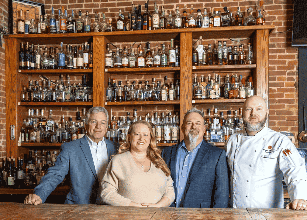 Four smiling people standing in front of shelves filled with bourbon bottles