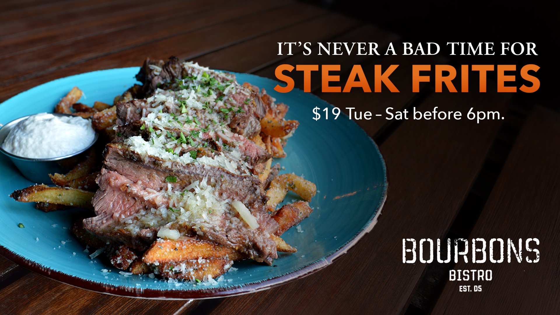 A round blue plate with a layer of seasoned French fries topped with sliced rare steak and garnished with parmesan. A ramekin of white horseradish sauce is on the side.