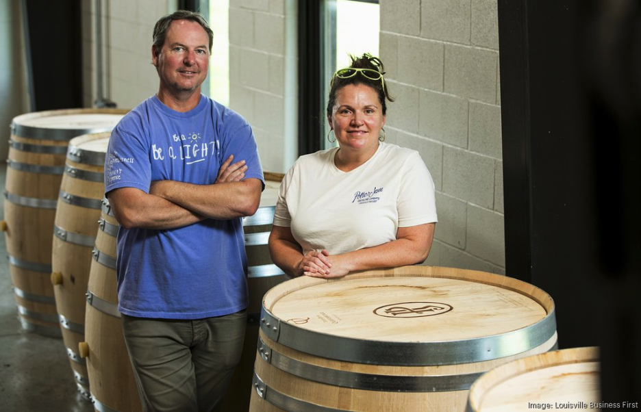 The founders of Potter Jane Distillery, Denny Potter and Jane Bowie, stand behind a large oak barrel.