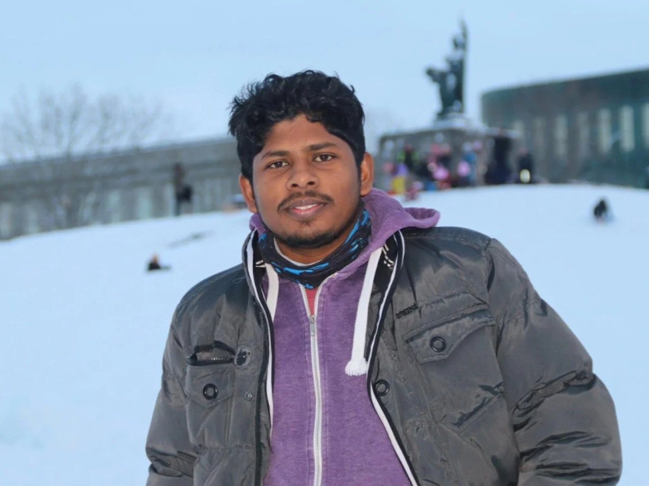 Gobi - senior researcher. A man posing outdoors in a snowy landscape with trees and a building in the background.