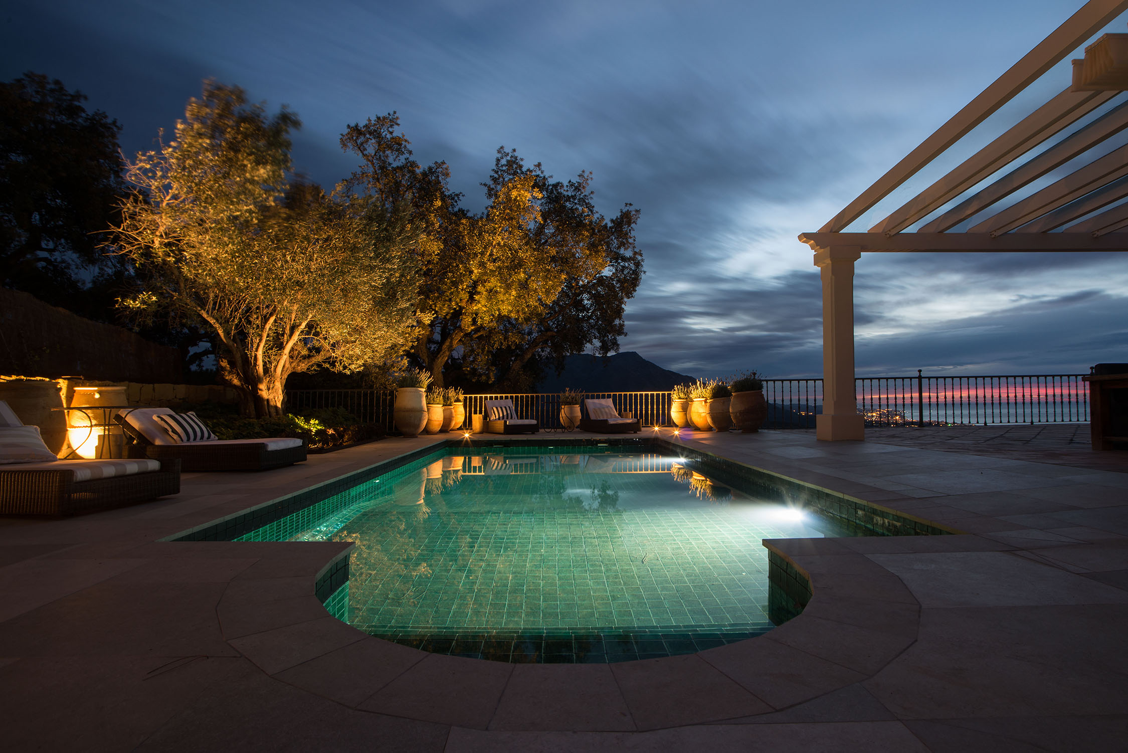 Luxurious outdoor pool area at dusk with lounge chairs, ambient lighting, and ocean view.