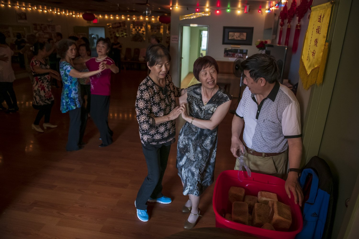 President of the Jiang Zhe Shanghai Association, Mr. Yuan Tao Di (right) hands out fresh bread during a dance event at a community hall in Chinatown. Since the mid-1990s, strong emigration of Mandarin-speakers from mainland China and other Chinese d