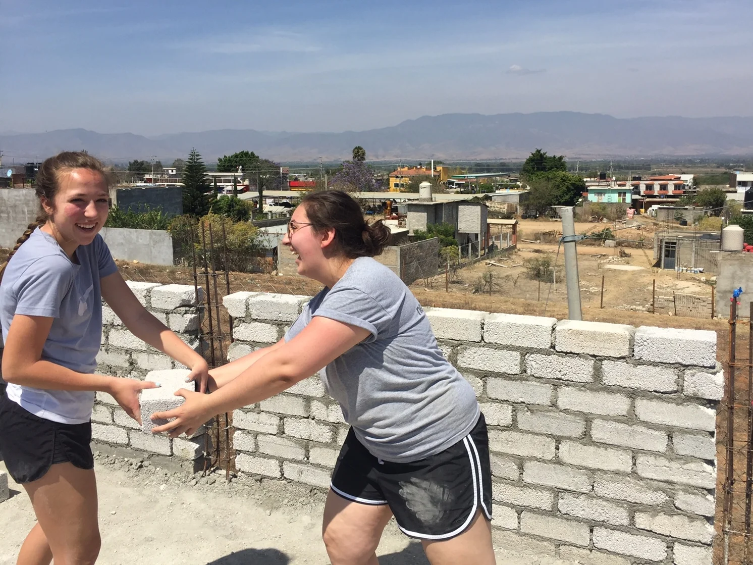 Camryn (left) and fellow volunteer, Katherine, pass cement bricks for an expansion of a patio at Casa Hogar Simply Smiles.