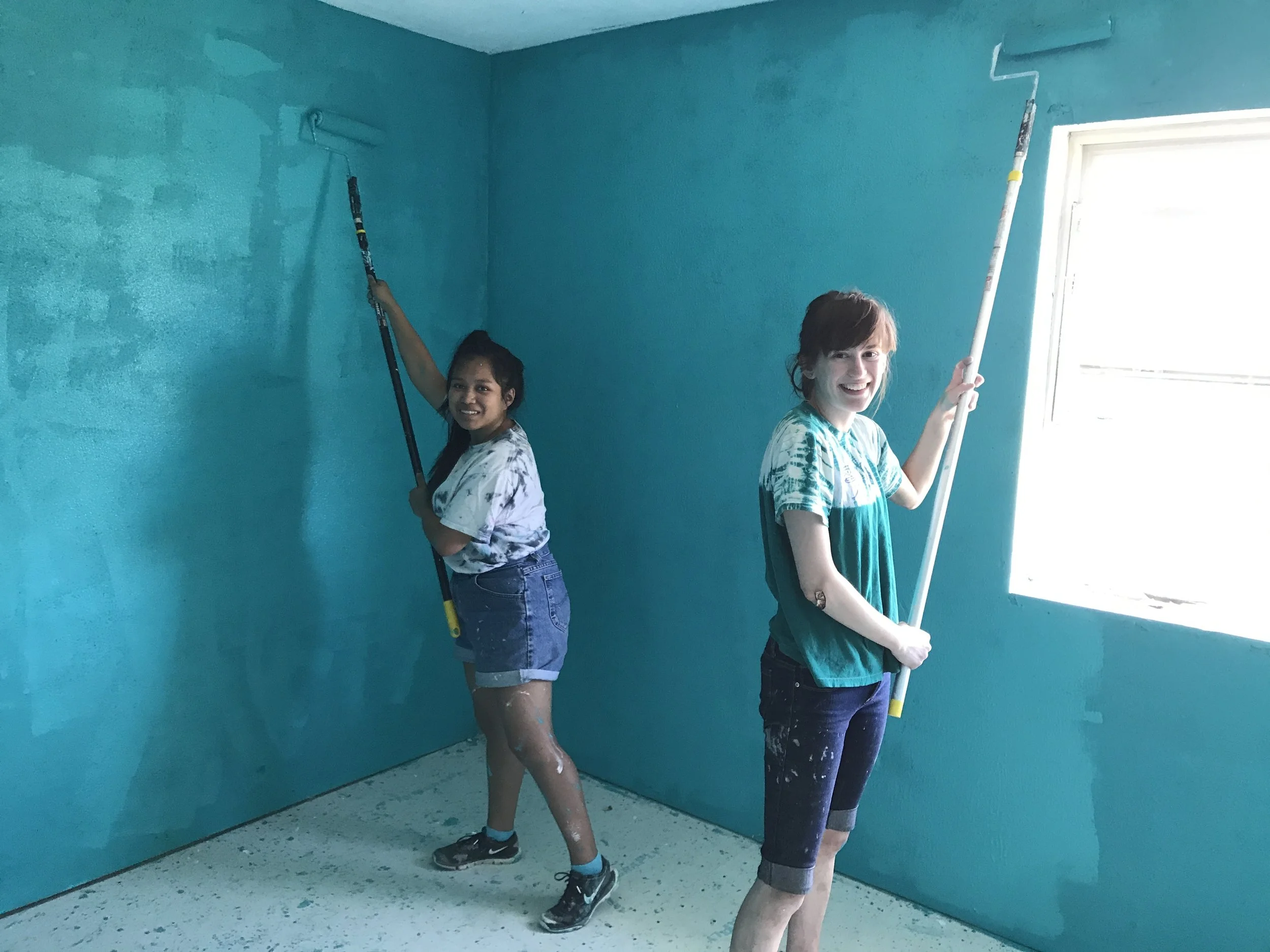 Volunteers Siona and Ruby work on painting the inside of a newly-renovated home of a community member.