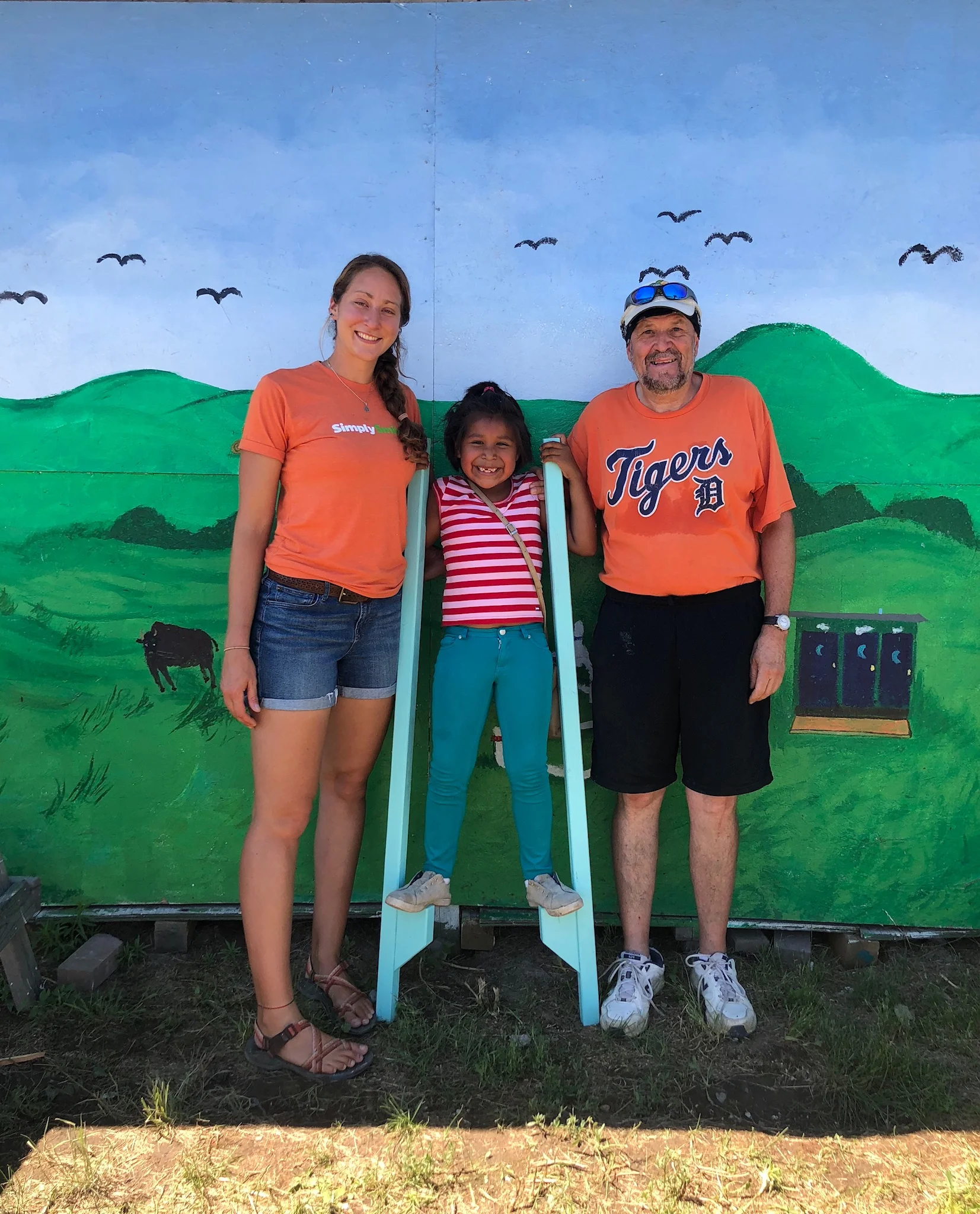 A little help from friends: Simply Smiles Volunteer Coordinator Sam Steinmetz and her high school basketball coach Al Ciarlo, who has volunteered on the Cheyenne River Sioux Tribe Reservation, help their young friend balance on newly constructed stilts at Simply Smiles Summer Camp.