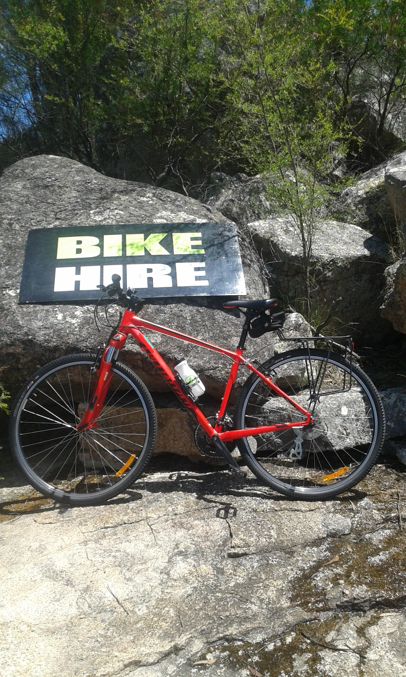 Red Specialized Crosstrail leaning again granite rock with bike hire sign behind.