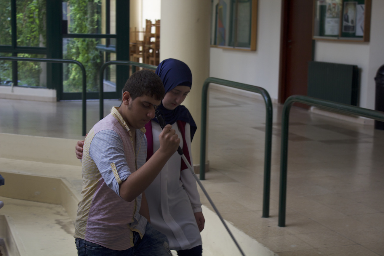 In the picture: a male Life Skill Program participant learns to use a white cane at the University of Balamand while walking with a female guide.