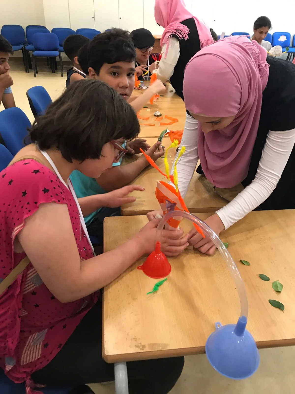 In the picture: A volunteer holds materials while a student creates a sculpture representing herself during an art class.