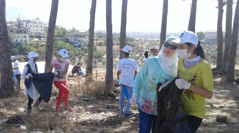 In the picture: a group of volunteers gather plastic items to be recycled using trash bags in a wooded area.