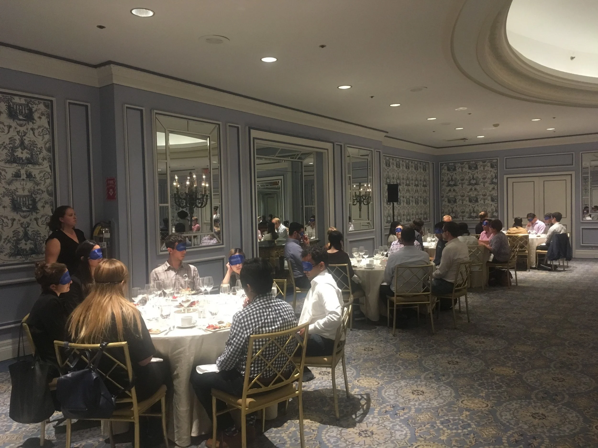 Room full of blindfolded participants sitting at tables discussing in groups