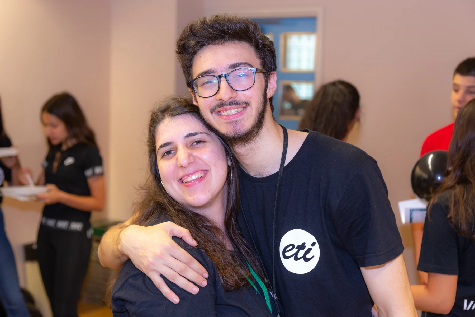 A man and a woman face the camera, smiling as they embrace each other.