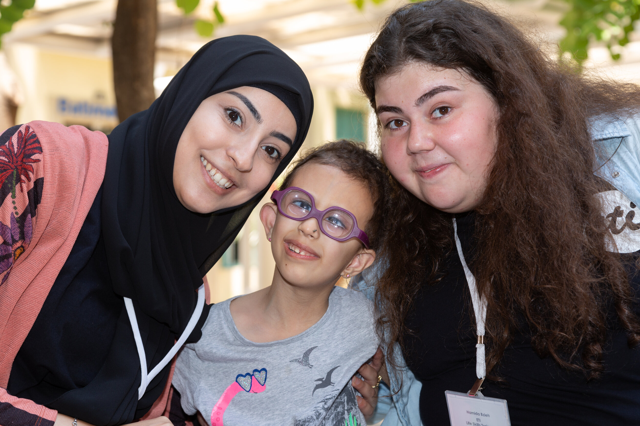 2 ETI volunteers pose with a young student who is smiling big