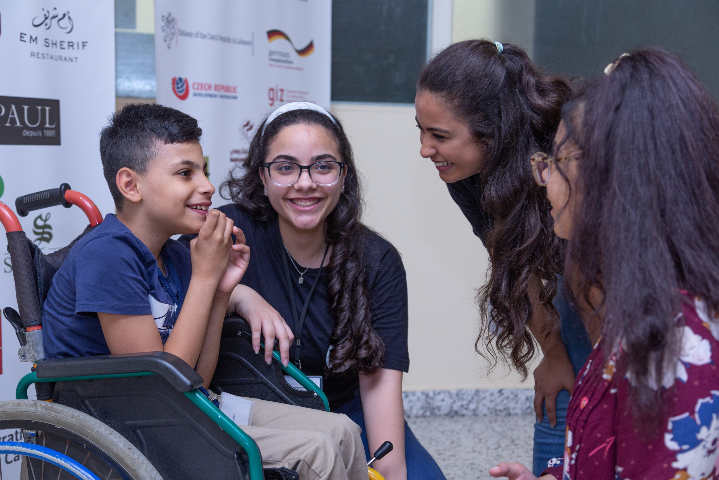 A volunteer converses with 2 young students, all are smiling
