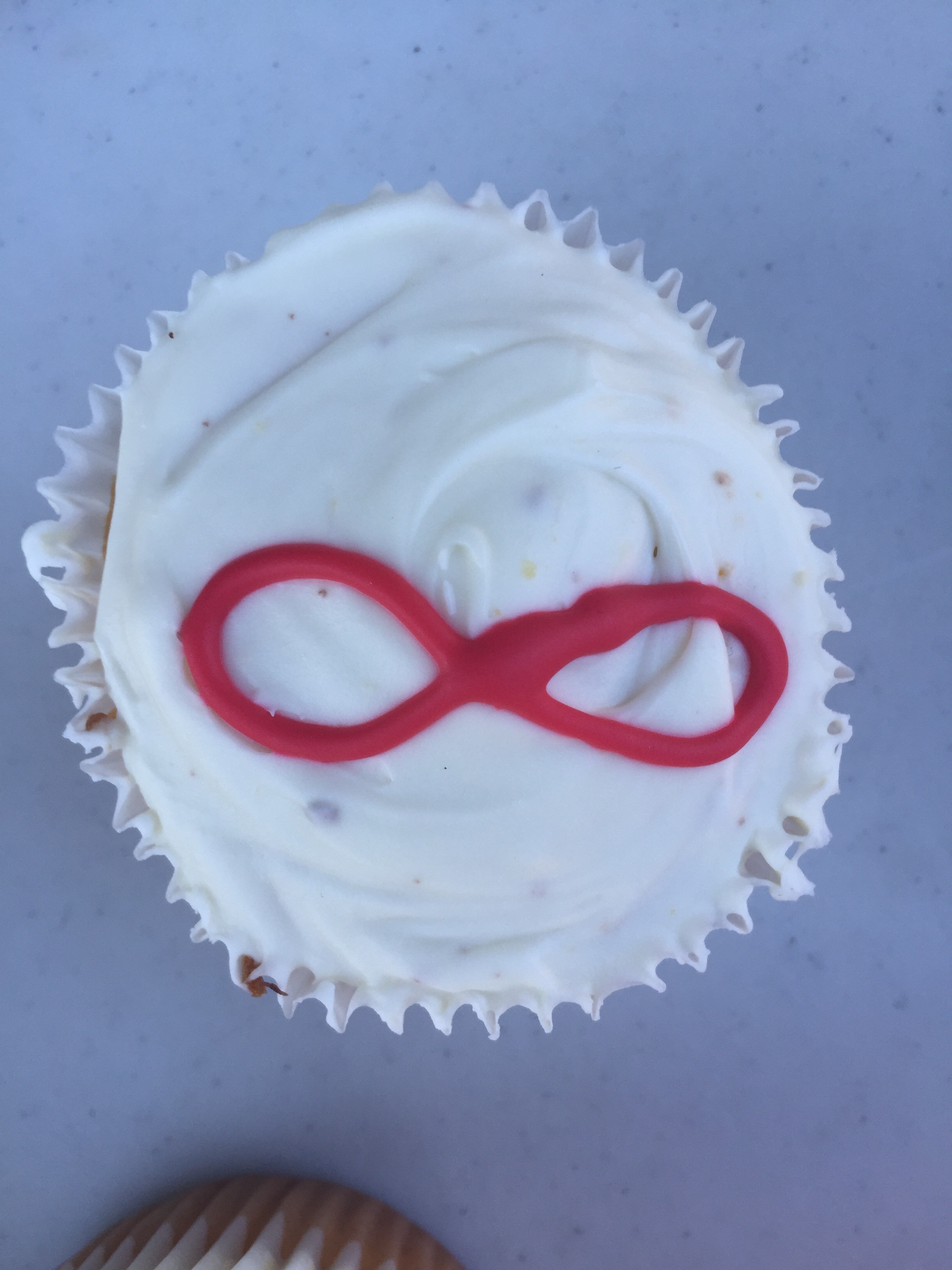 Image description: A cupcake with white frosting and a red infinity symbol in the center.