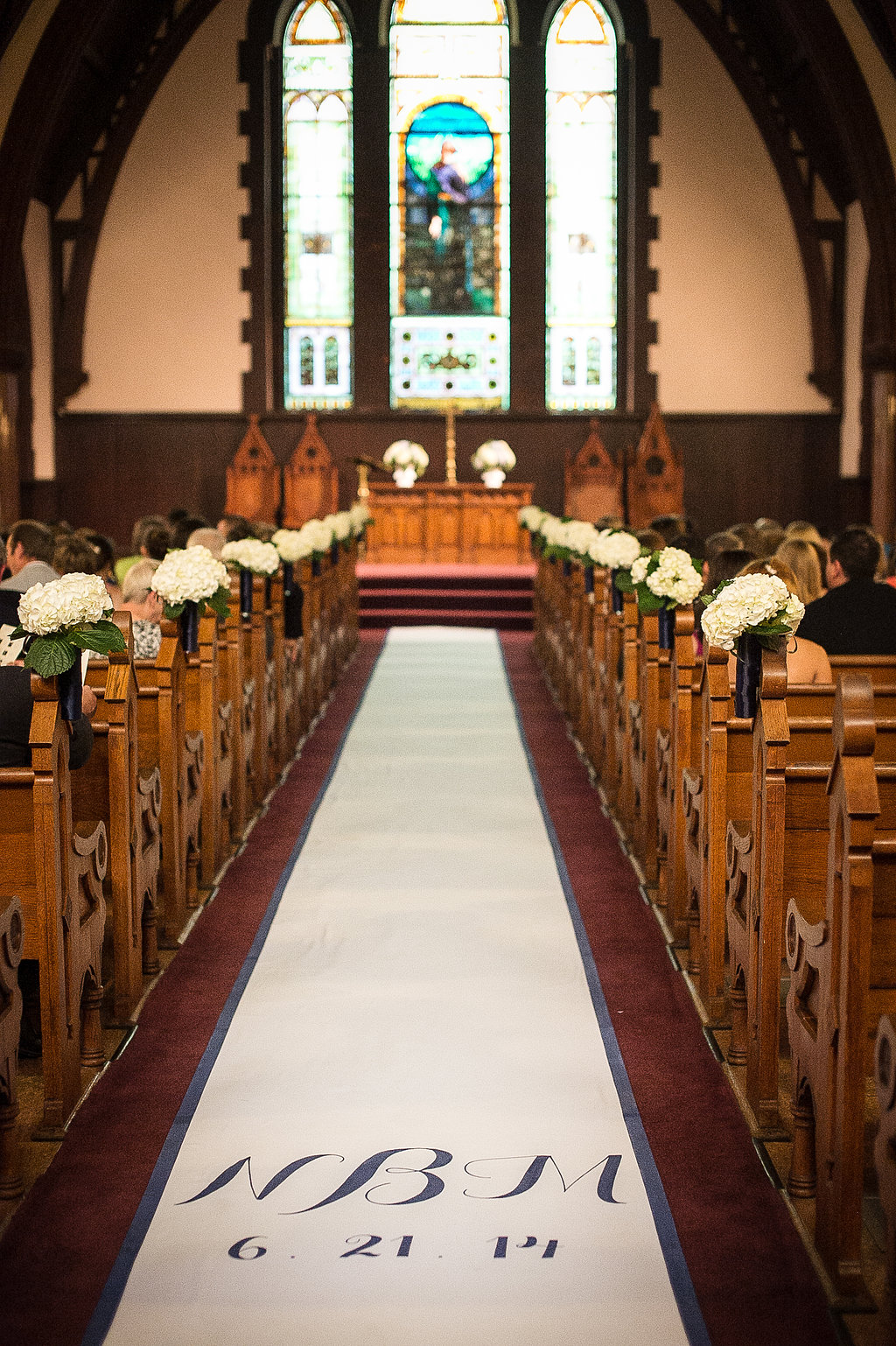 In the church we did a custom aisle runner in white with simple navy script of the couple's initials and the date, we did a navy stripe going down the sides of the aisle to keep with the theme, and mini bouquets of white hydrangeas lining the pews to create an elegant pathway for the bride.