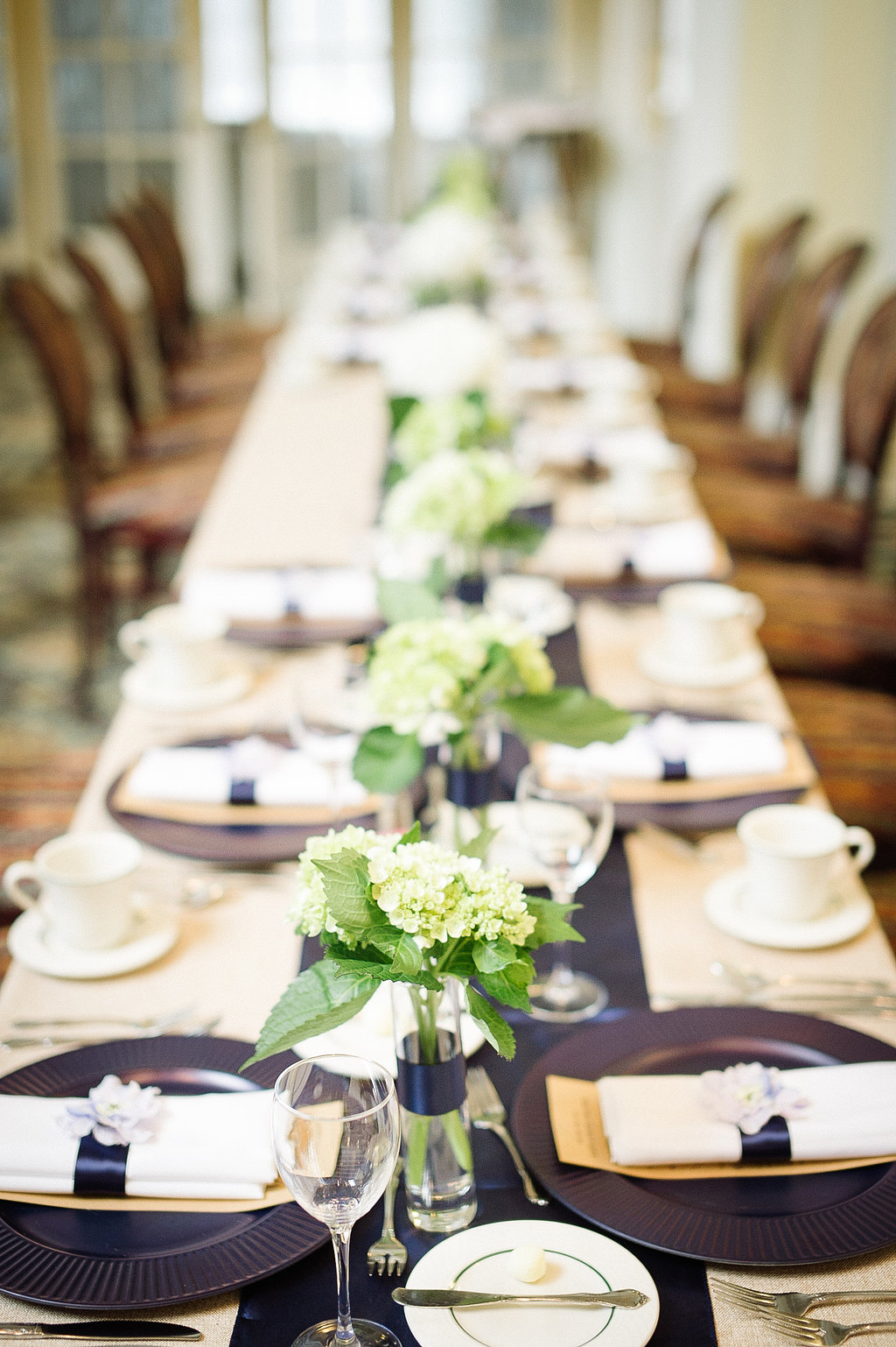 For this wedding the bride and groom did a modified head table, so we did small cylinder bud vases with a stripe of satin navy ribbon filled with small bouquets of green and white hydrangea over a matching navy satin runner.