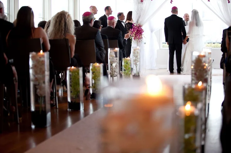 We did a simple white aisle runner for the bride and lined it with tall square vases with submerged cymbidium orchids in whtie and green over river rocks topped with a&nbsp; floating candle to create&nbsp; simple elegant pieces to line the aisles wi…
