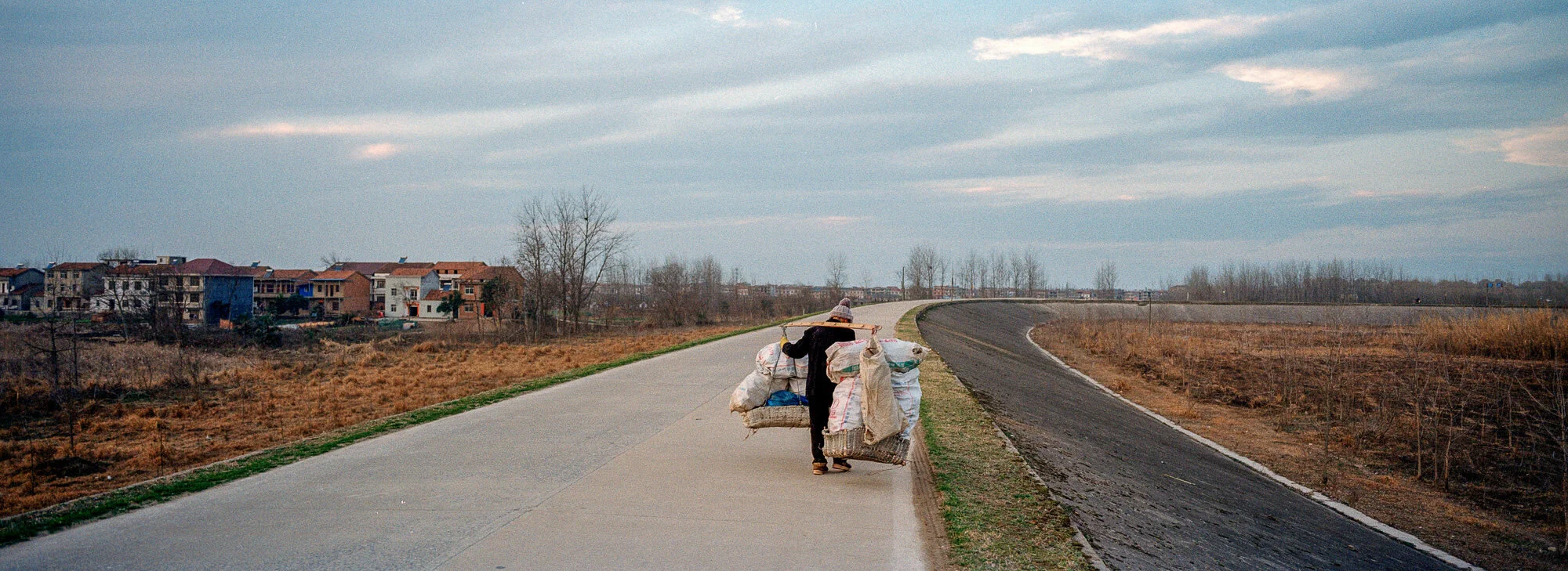  February 24, 2018, Xiaoxhizhen, A man carries a heavy load balanced across his back with a bamboo pole. 