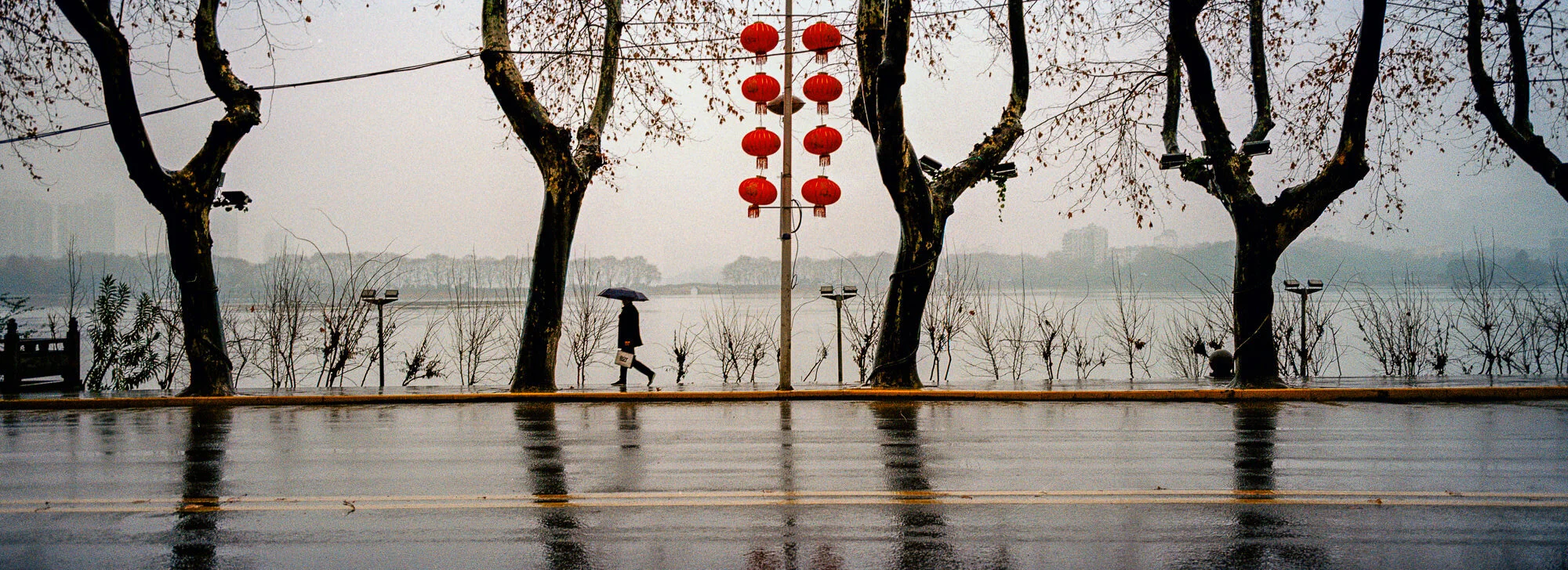  February 23, 2018, Jiujiang, Jiangxi Province - A man walks under an umbrella next to a lake in the city’s downtown on a rainy morning.  