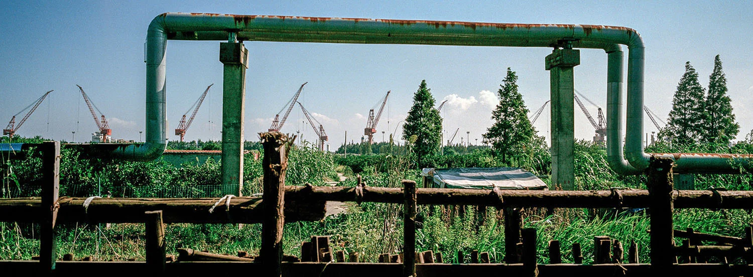  August 5, 2018, Shanghai, China - A fence, water pipes, farmland and cranes of shipyards on Changxing Island in the mouth of the Yangtze River.  