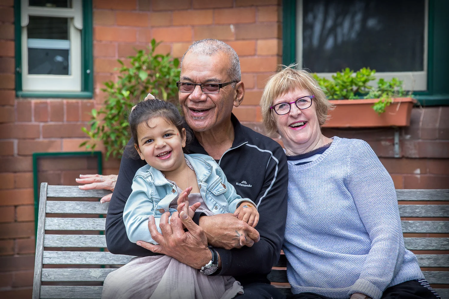 Young girl sitting on grandparents knee on garden bench
