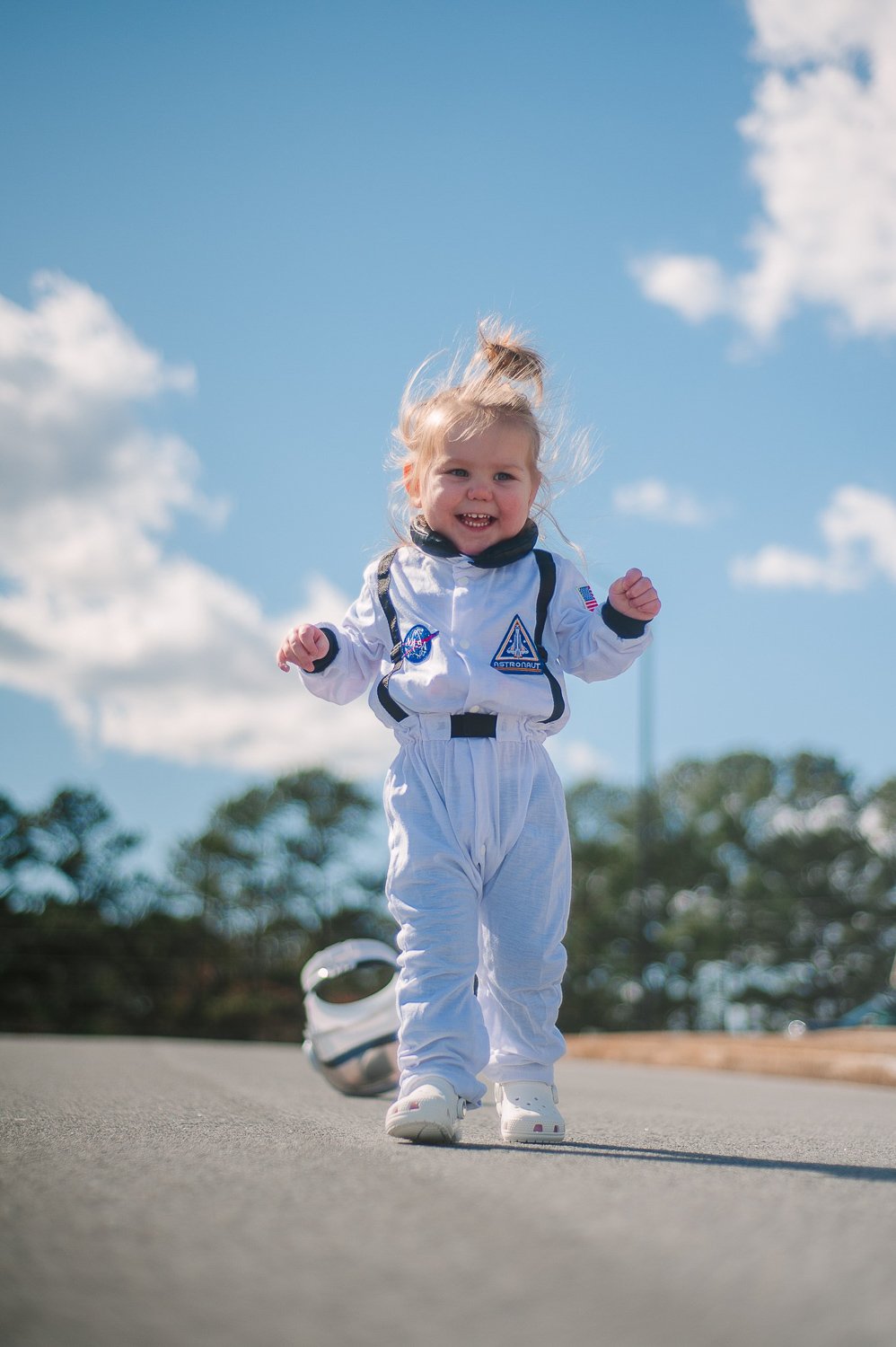 A little blonde girl standing outside wearing a white space suit 