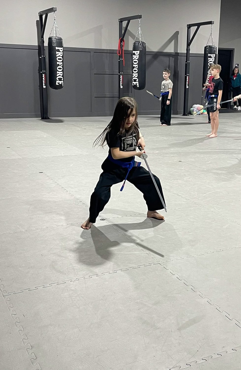 A young girl in martial arts outfit wielding a sword inside a gymnasium  