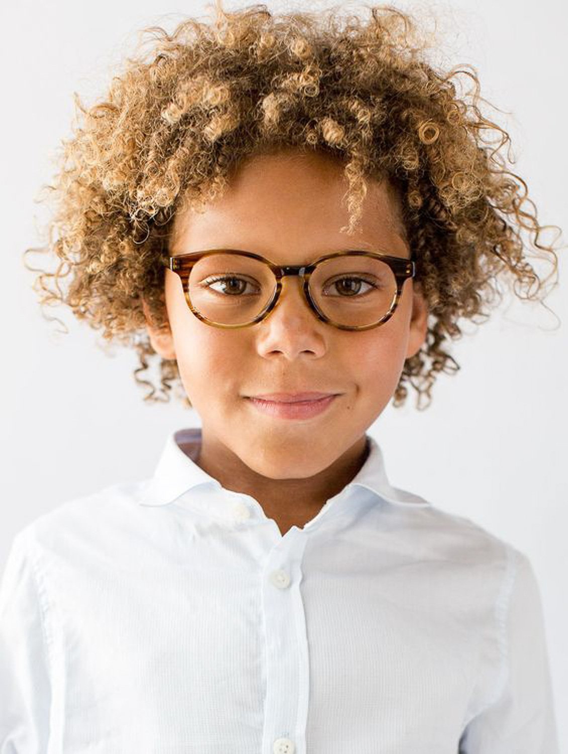 A close up of young boy with curly brown hair wearing glasses 