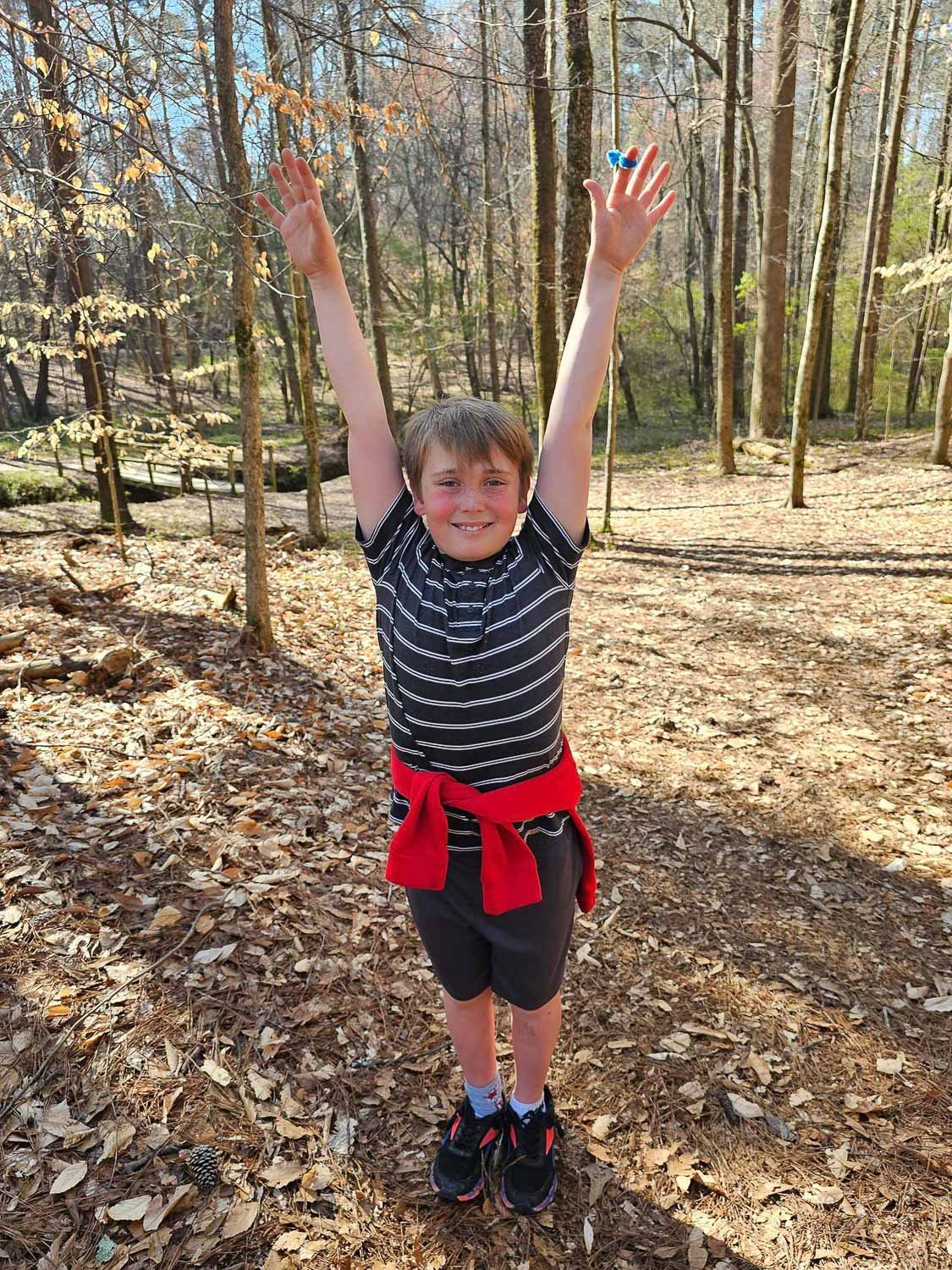 A young boy standing in a park with hands in the air