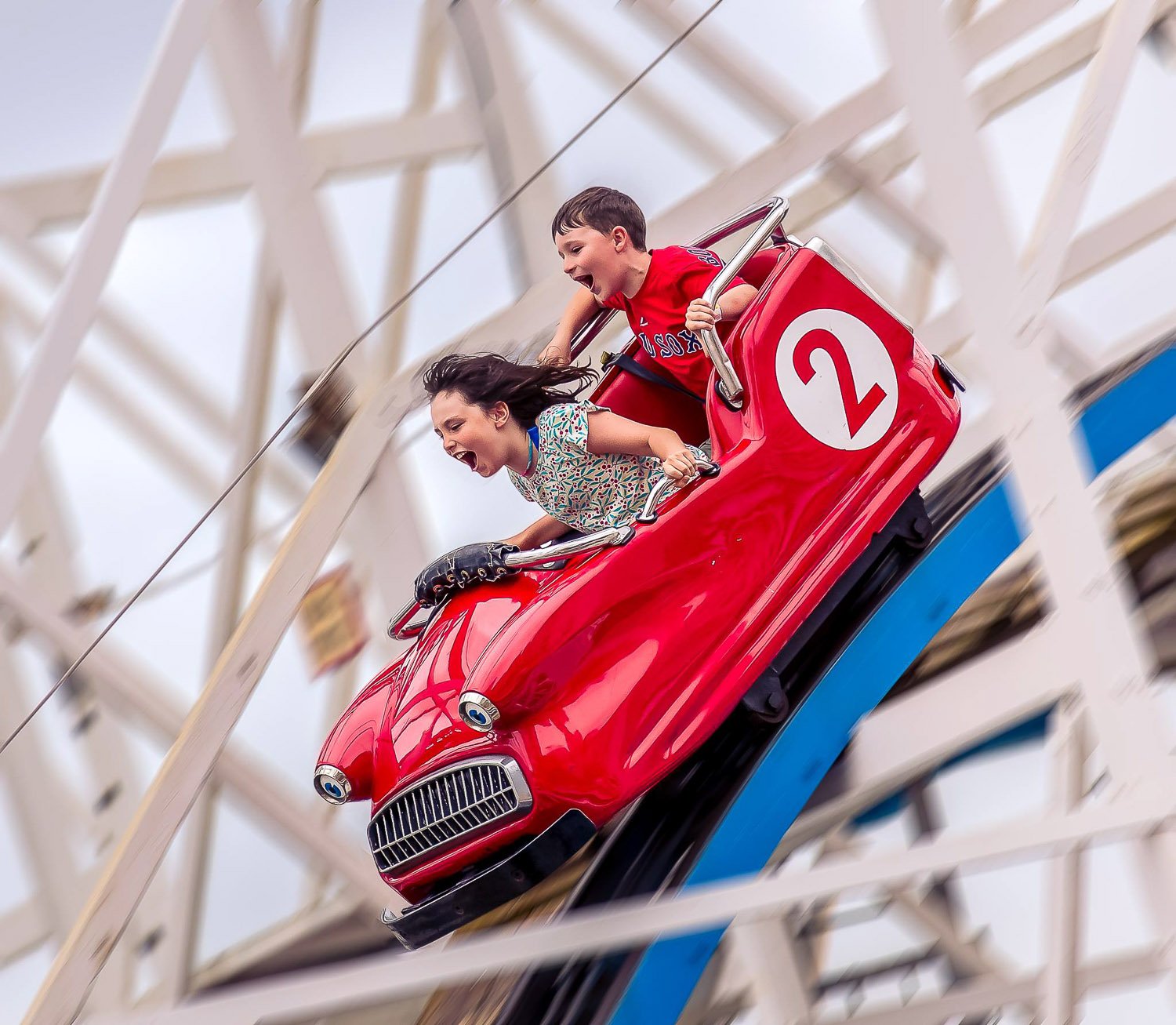 A boy and girl in a red roller-coaster car