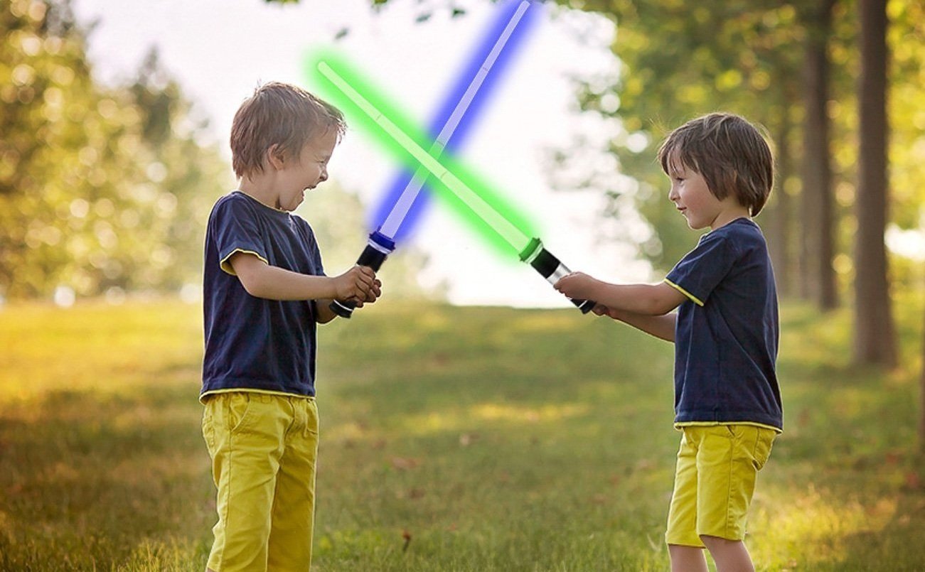 Two young boys playing outside with toy lightsabers