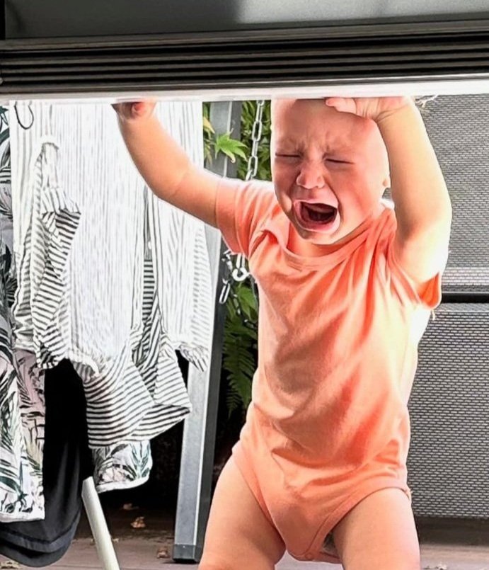 A toddler boy crying with his hands in the air