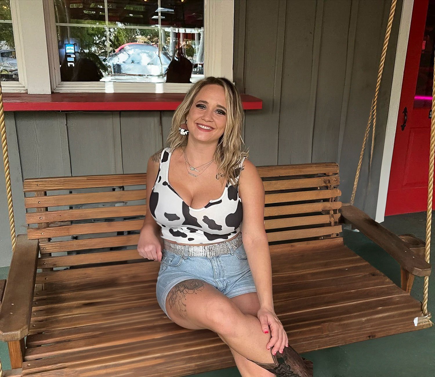 A blonde woman sitting on a wooden bench smiling at camera