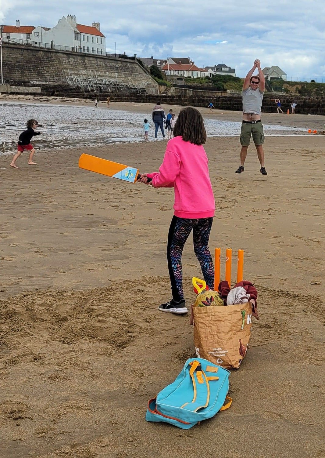 A family of three playing cricket on a beach