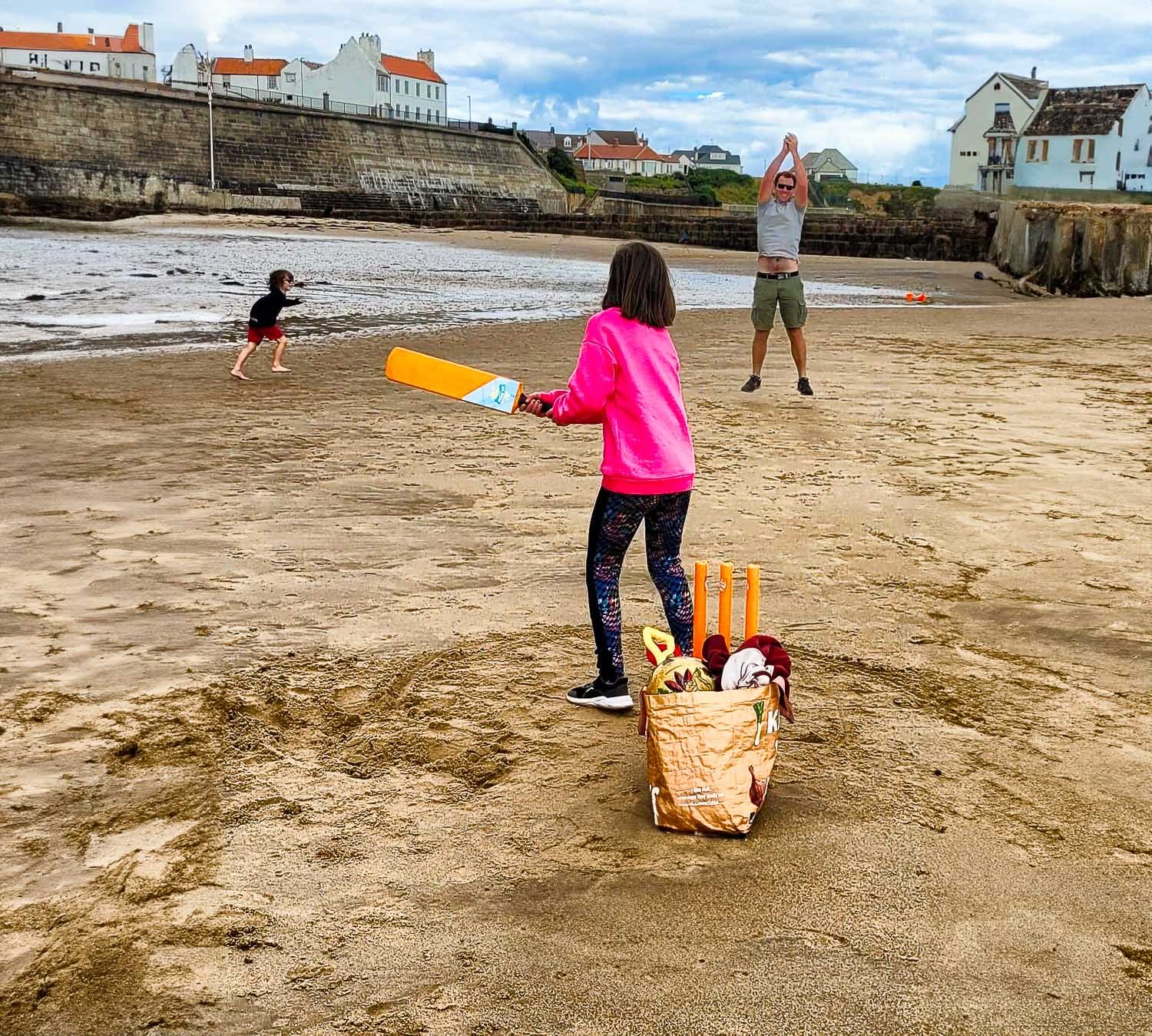 A family of three playing cricket on the beach