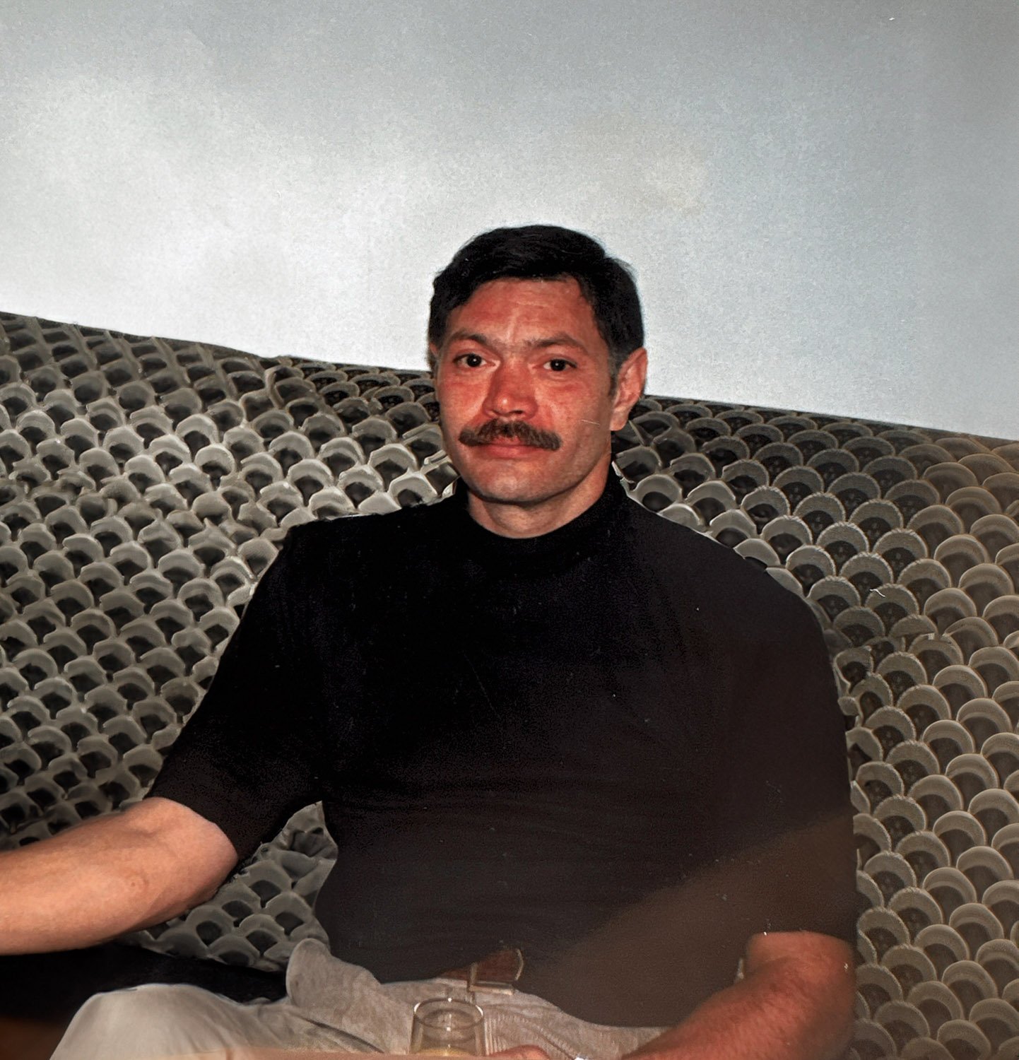 A man in a black shirt sitting inside on a couch