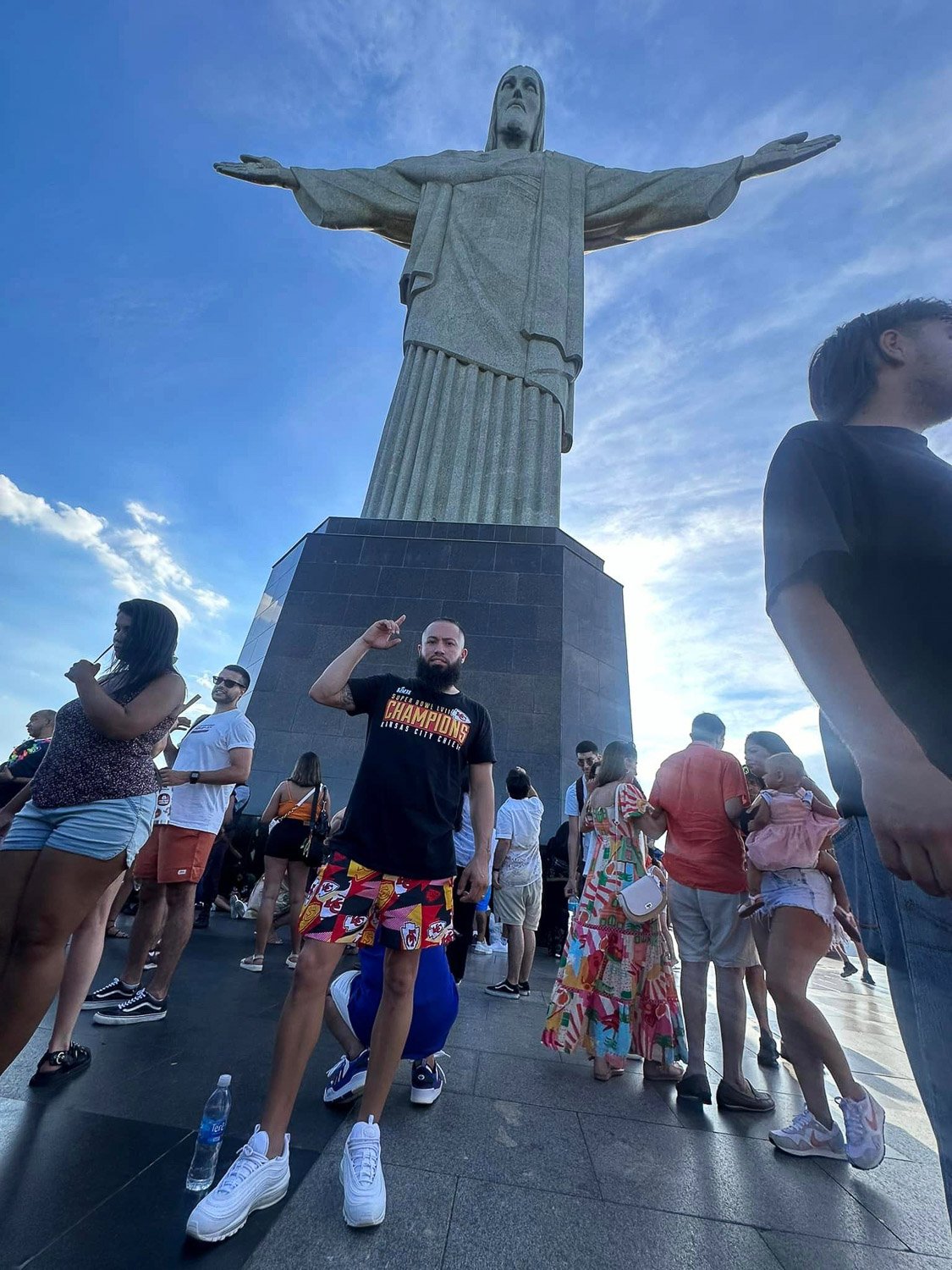 A man posing in a crowd in front of the Christ the Redeemer statue