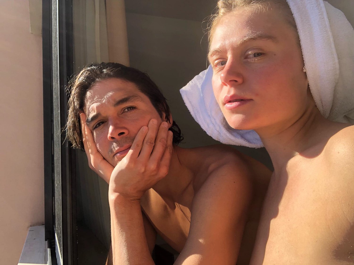 A topless couple staring out of a sunlit window