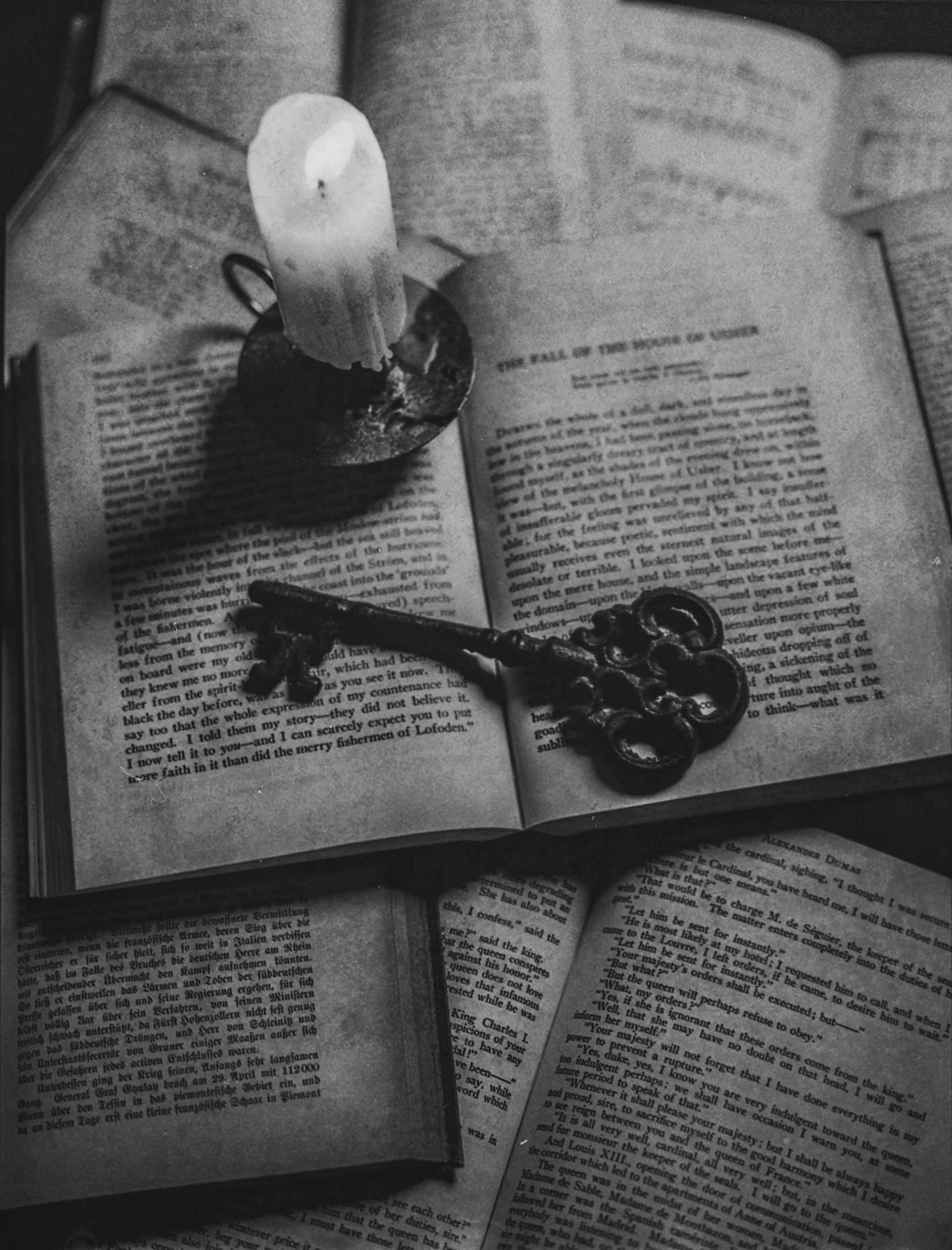 An open book with a lit candle in a holder and an ornate antique key resting on the pages.