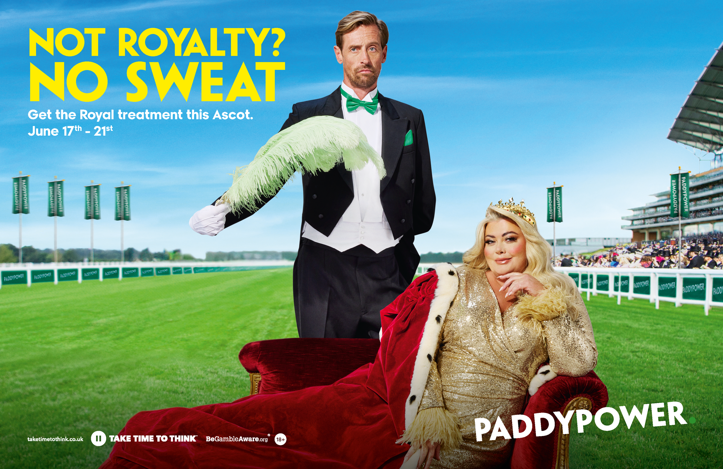 A man in a tuxedo with a green bow tie and pocket square holding a large pale green feather, standing next to a seated woman in a gold dress with a fur coat and crown, on a racecourse with green banners and a blue sky.