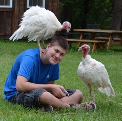 Jake Clements with two white turkeys in a field.