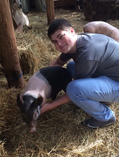Jake Clements holding a pig in some hay.