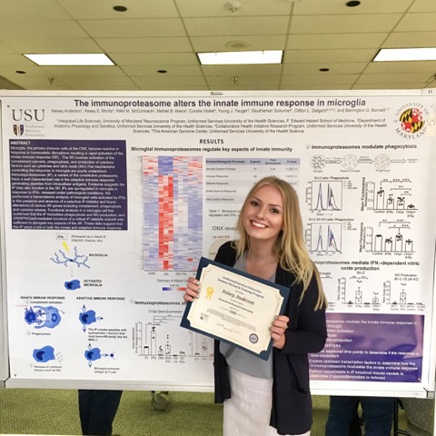 Kelsey Anderson in front her award-winning poster at a symposium at Uniformed Services University Health Services (USUHS)