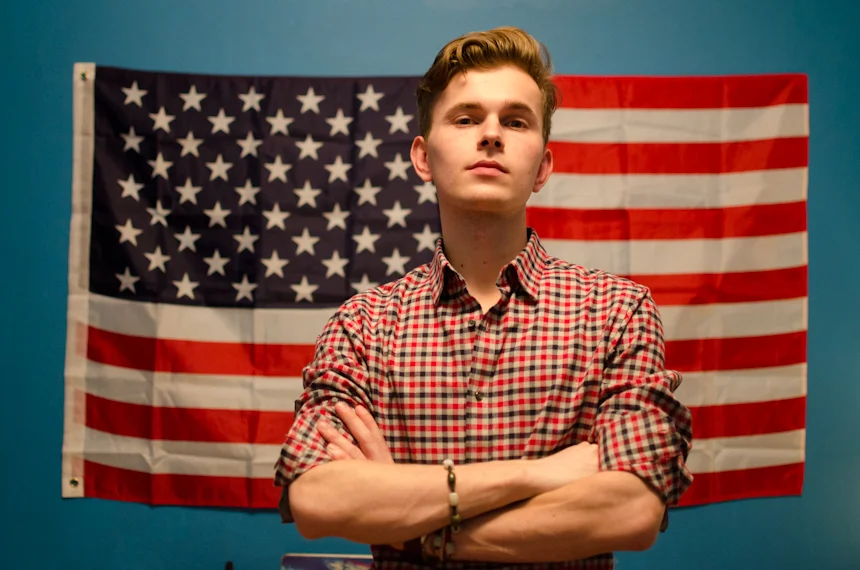 Philipp Shchekin, a Russian gay asylum seeker from Vladivostok, stands in front of the American flag he hangs in his shared one-bedroom apartment in Brooklyn, New York. 