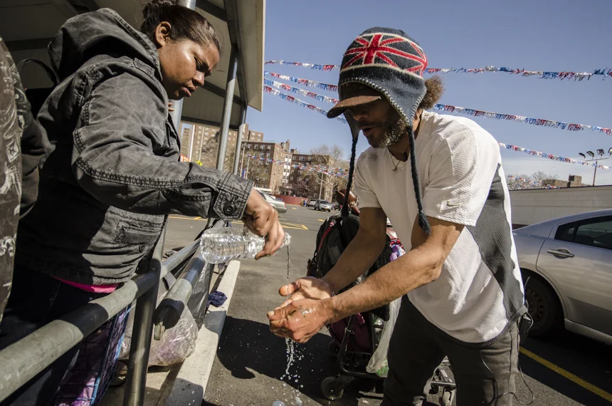 At the recycling center in South Bronx, José washes his hands with laundry soap. His friend Princess pours water on them to help him wash the soap off.