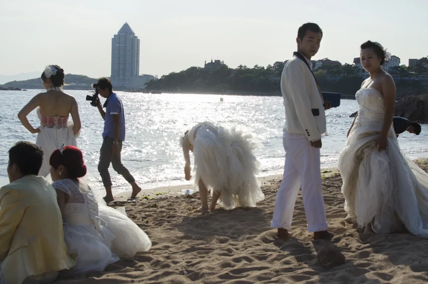 A few pairs relax on the beach in photo-ready costumes, waiting for the photographer to call their turn. They are all from Hebei Province and came to Qingdao on a pre-arranged "wedding-bus" full of other couples. Because Qingdao is a hot destination for vacations, many photo studios from inland China have started offering combo packages that bundle the shoot with a travel plan that give the couples one or two extra days to tour the city. According to local newspaper, n early one third of couples having their photos taken on the coastline of Qingdao is from outside the city and sometimes even outside Shandong Province. 